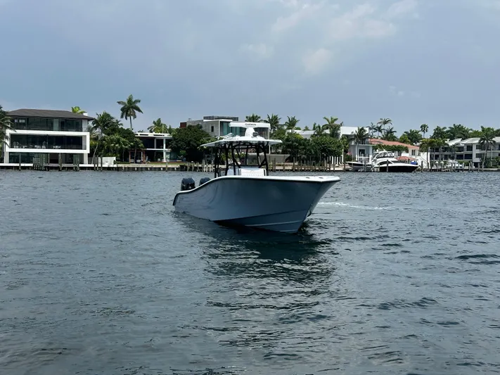  Yacht Photos Pics 2024 Yellowfin 34 Offshore boat cruising near waterfront homes under a cloudy sky.