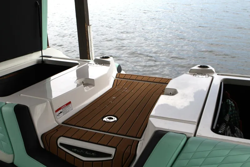  Yacht Photos Pics 2024 Nautique Super Air Nautique G23 boat deck with open storage compartments by the water.