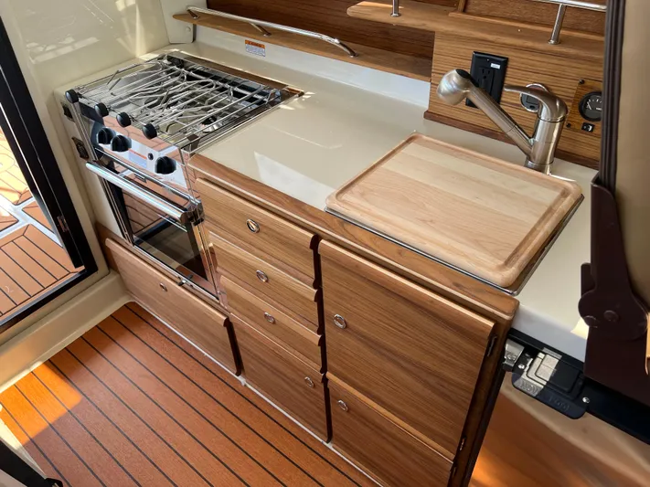  Yacht Photos Pics 2024 Ranger Tugs R-27 kitchen with stove, wooden cabinetry, and cutting board.