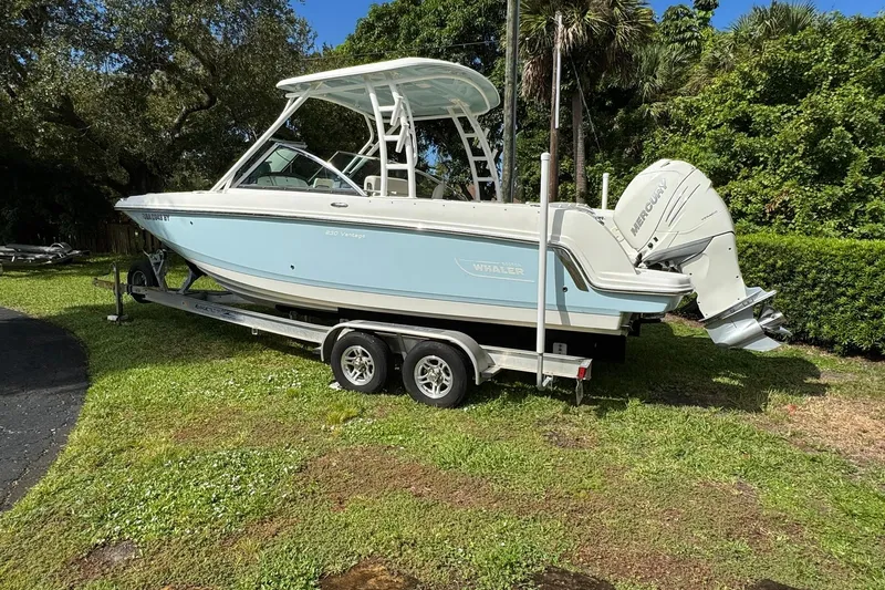  Yacht Photos Pics 2019 Boston Whaler 230 Vantage boat on trailer, parked on grass with trees in background.