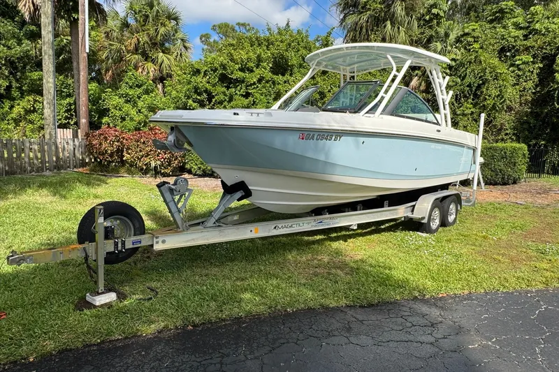  Yacht Photos Pics 2019 Boston Whaler 230 Vantage boat on trailer, parked on grass with lush greenery background.