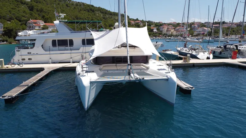  Yacht Photos Pics 2023 Lagoon 42 catamaran docked in a marina, surrounded by other boats.