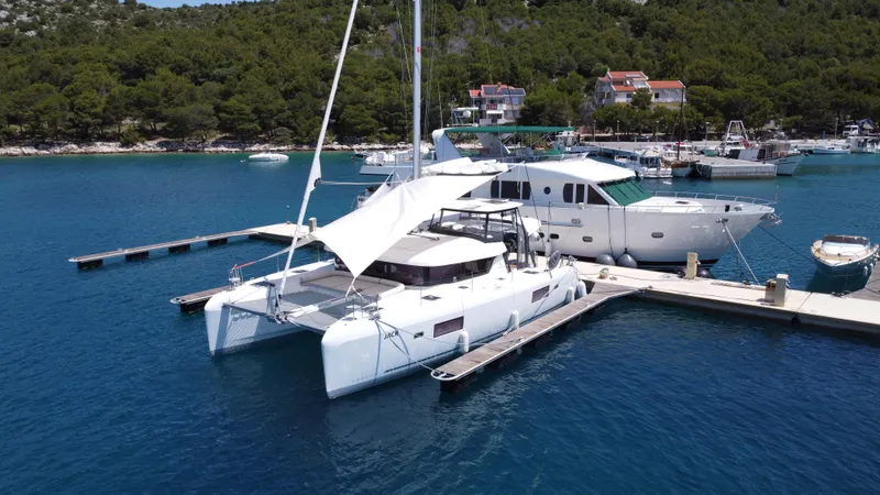  Yacht Photos Pics 2023 Lagoon 42 catamaran docked in a scenic marina with lush greenery.