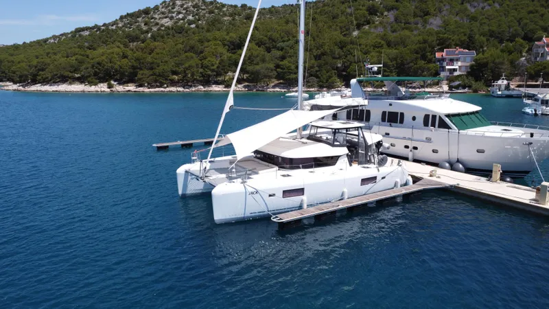  Yacht Photos Pics 2023 Lagoon 42 catamaran docked in a scenic marina with lush greenery.