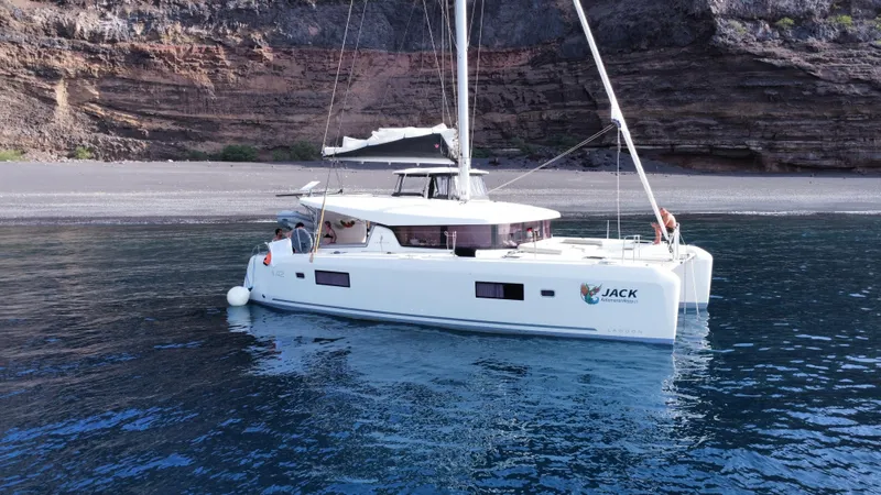  Yacht Photos Pics 2023 Lagoon 42 catamaran anchored near rocky shoreline, calm blue waters.