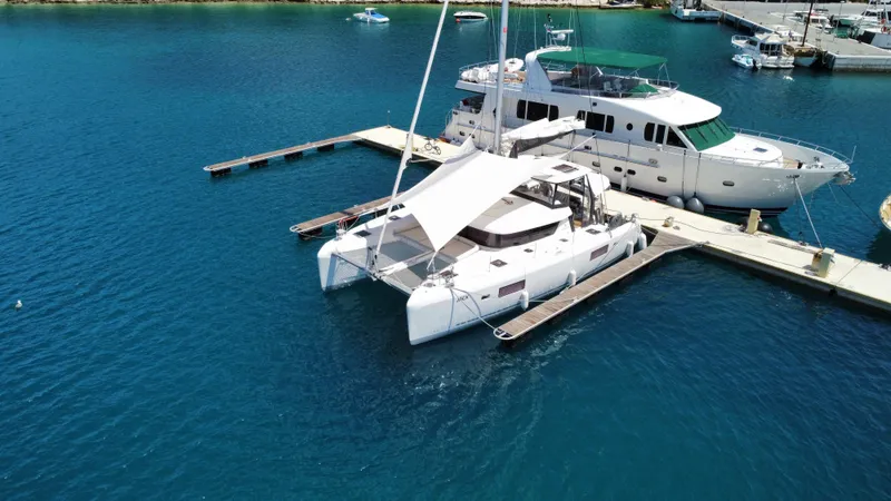  Yacht Photos Pics 2023 Lagoon 42 catamaran docked at marina, surrounded by clear blue water.