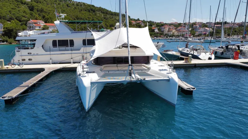  Yacht Photos Pics 2023 Lagoon 42 catamaran docked in a scenic marina with clear blue water.
