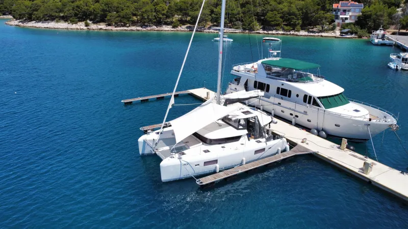  Yacht Photos Pics A 2023 Lagoon 42 catamaran docked beside a yacht in a serene marina.