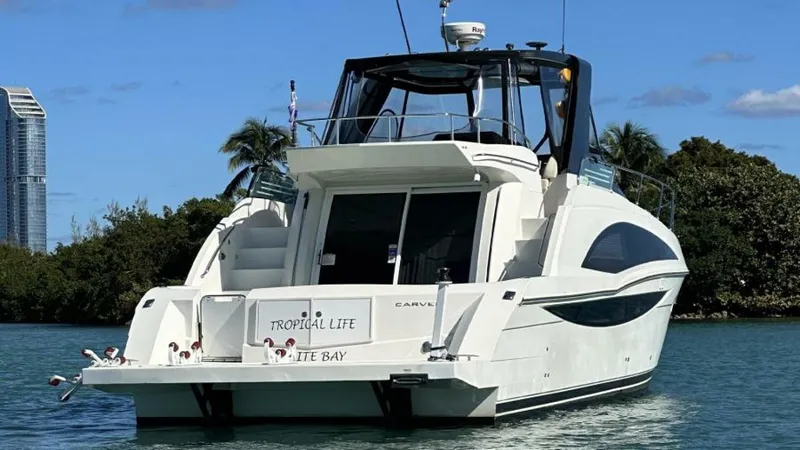Tropical Life Yacht Photos Pics 2012 Carver Sojourn yacht on water, surrounded by trees and buildings, under a clear sky.