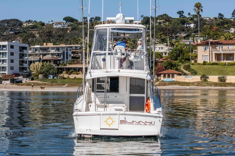 Sunny 1 Yacht Photos Pics 2001 Riviera 36 Flybridge boat on calm water near a scenic coastal town.