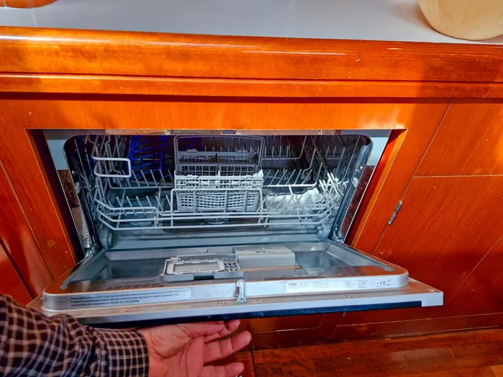  Yacht Photos Pics Open dishwasher in a 2004 Beneteau 57 yacht kitchen, showcasing interior racks and wooden cabinetry.