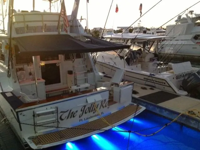 The Jolly Rogers Yacht Photos Pics 1987 Hi-Star Sportfish boat docked with blue underwater lights at sunset.