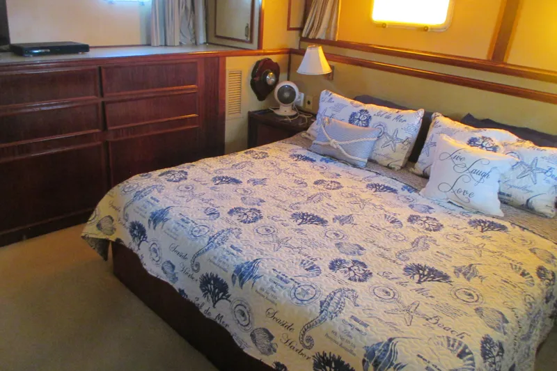 Hattitude Yacht Photos Pics Cozy bedroom in 1981 Hatteras 61 Motor Yacht with nautical-themed bedding and wooden cabinetry.