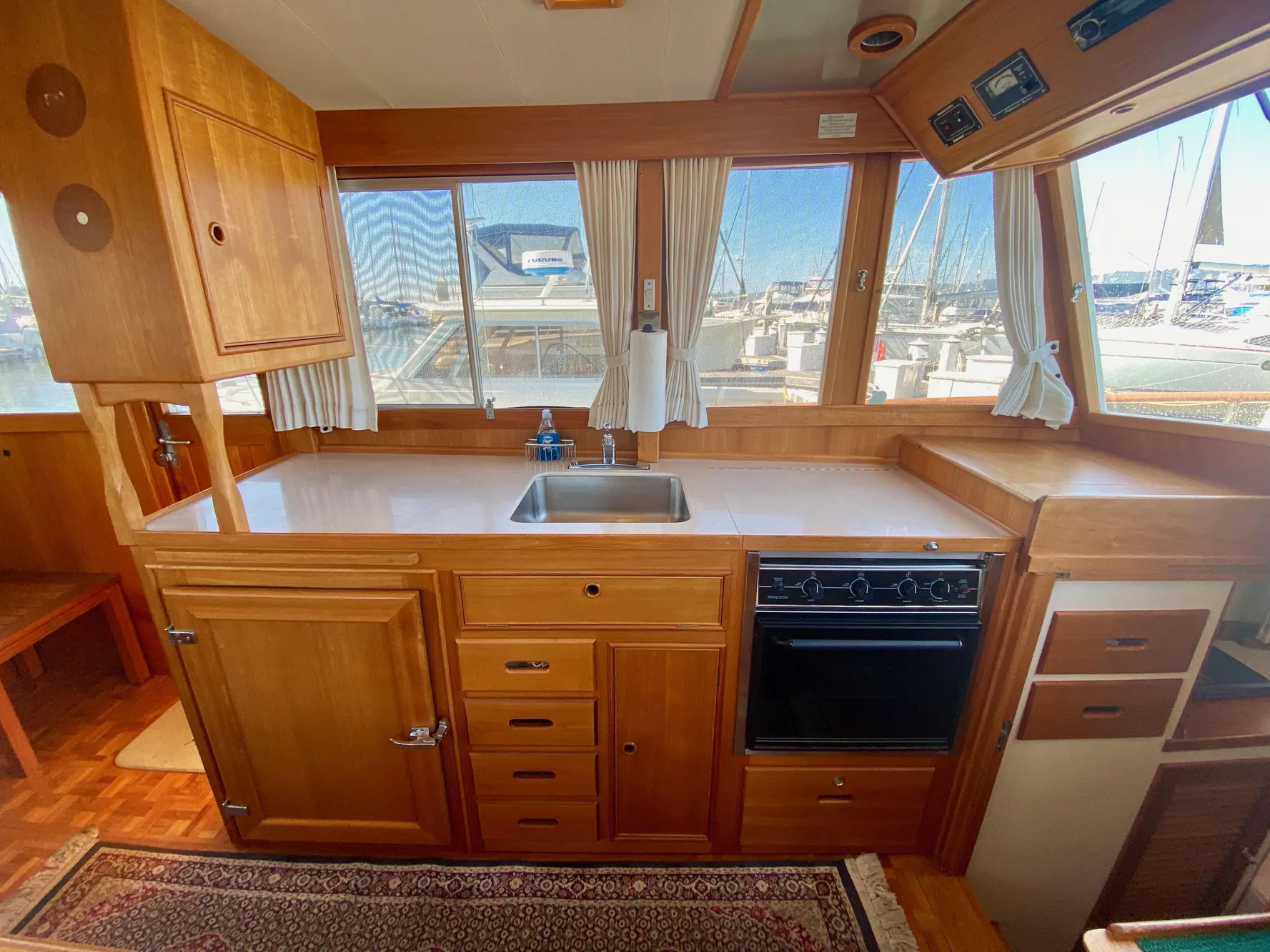 1997 Grand Banks Classic yacht kitchen with wooden cabinetry, sink, and stove, overlooking marina.