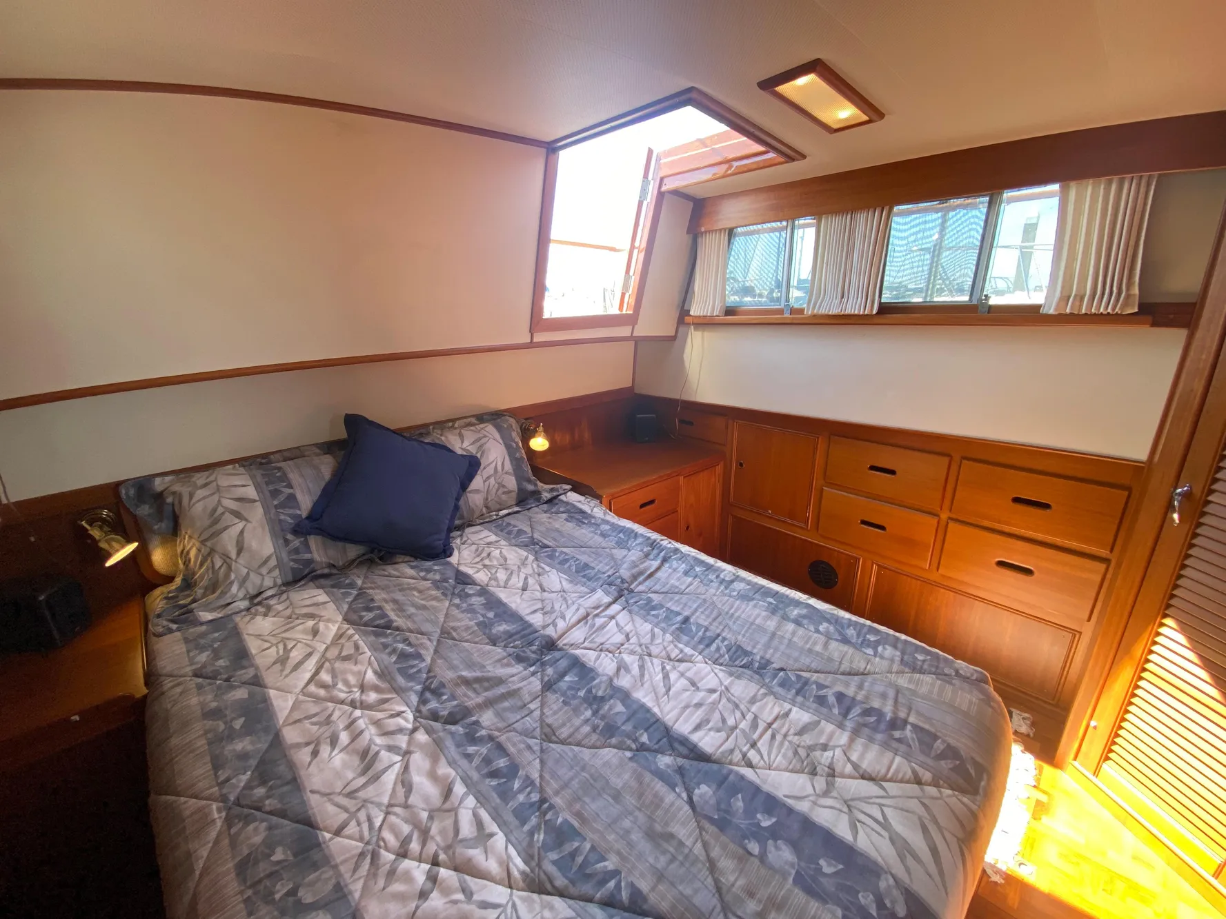 Cozy bedroom in 1997 Grand Banks Classic yacht with wood cabinetry and natural light.