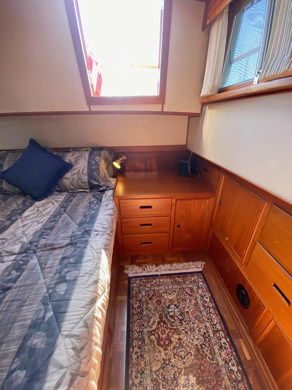 Cozy cabin interior of 1997 Grand Banks Classic yacht with bed, wooden cabinetry, and rug.