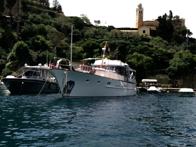  Yacht Photos Pics Classic 1965 Feadship Caravelle 23 yacht docked near lush greenery and historic building.
