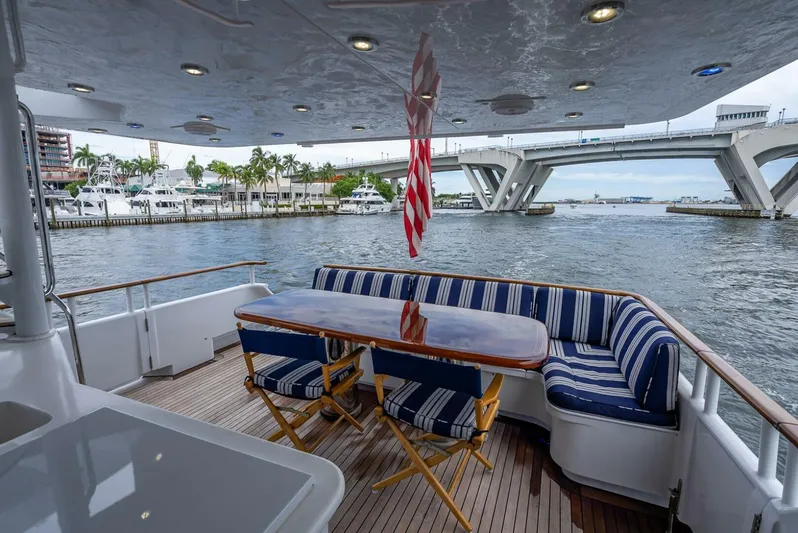 Lady Helen Yacht Photos Pics Luxury yacht deck with striped seating, wooden table, and waterfront view. Broward 87, 1982 model.