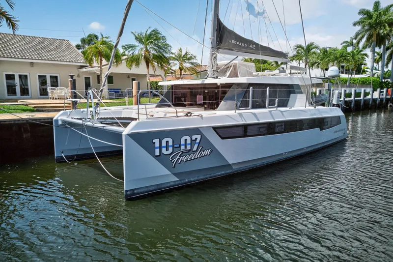 Ten-seven Freedom Yacht Photos Pics 2023 Leopard 42 catamaran docked by waterfront home, featuring "10-07 Freedom" on hull.