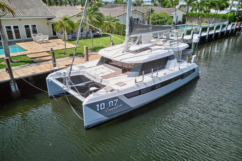 Ten-seven Freedom Yacht Photos Pics 2023 Leopard 42 catamaran docked by waterfront home with pool and palm trees.