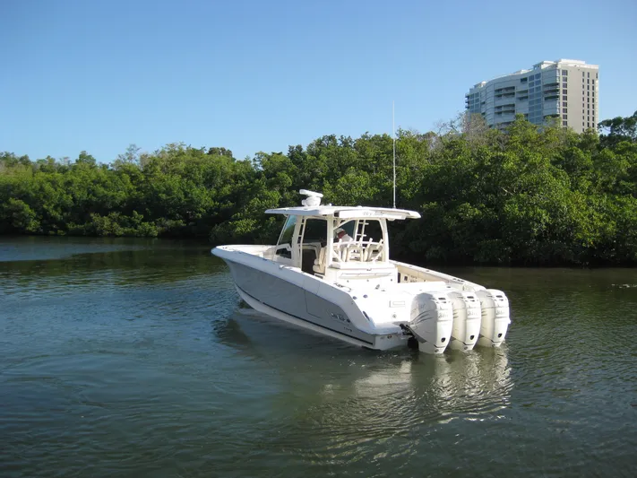  Yacht Photos Pics 2018 Boston Whaler 380 Outrage boat on calm water near lush greenery and buildings.