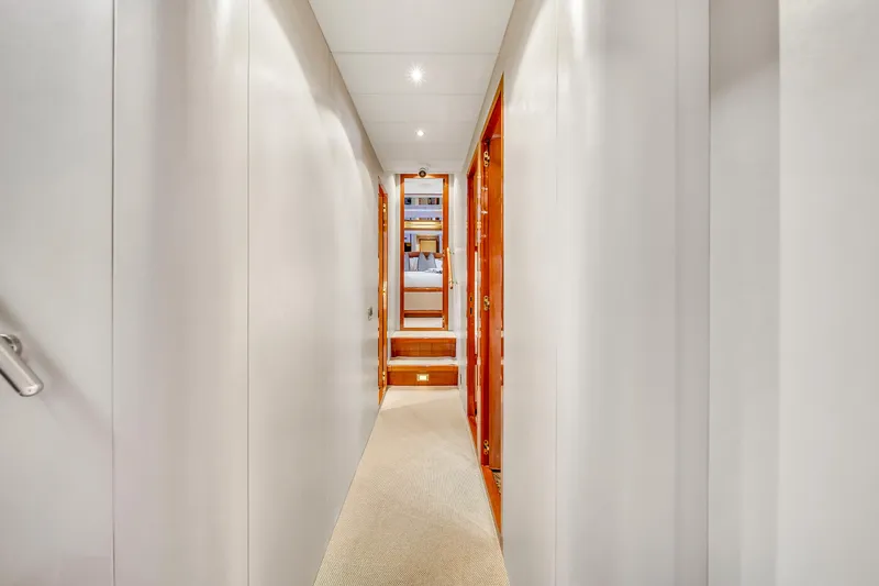  Yacht Photos Pics Narrow hallway inside 2002 Mangusta 108 yacht, featuring sleek white walls and wooden accents.