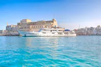 Luxury yacht by historic fort, clear blue water, sunny day, 1982 Husumer Shipyard model.