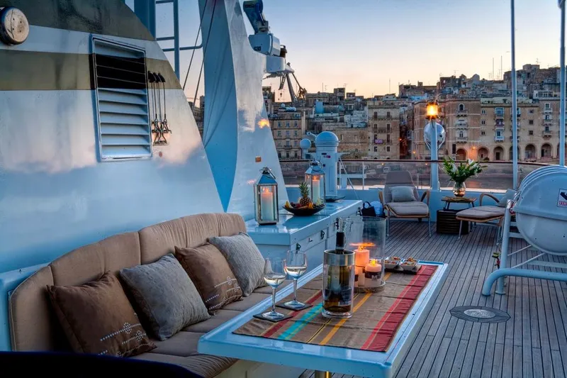 Sanssouci Star Yacht Photos Pics Luxurious yacht deck with cozy seating, candles, and cityscape view at sunset. Custom Husumer Shipyard, 1982.