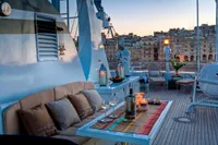 Luxurious yacht deck with cozy seating, candles, and cityscape view at sunset. Custom Husumer Shipyard, 1982.
