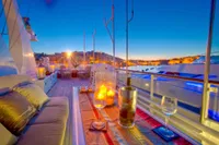 Luxurious yacht deck at sunset with candles, wine glasses, and cityscape view.