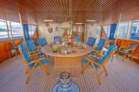Luxurious yacht interior with round table, blue-striped chairs, and wooden decor, Custom Husumer Shipyard 1982.
