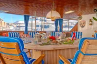 Luxurious yacht dining area with blue-striped chairs, wooden table, and nautical decor, 1982 Husumer Shipyard.