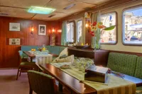 Cozy ship dining area with wooden decor, green seating, and floral arrangements, Husumer Shipyard 1982.