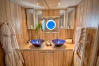 Luxurious ship bathroom with dual blue glass sinks, wooden paneling, and plush robes.
