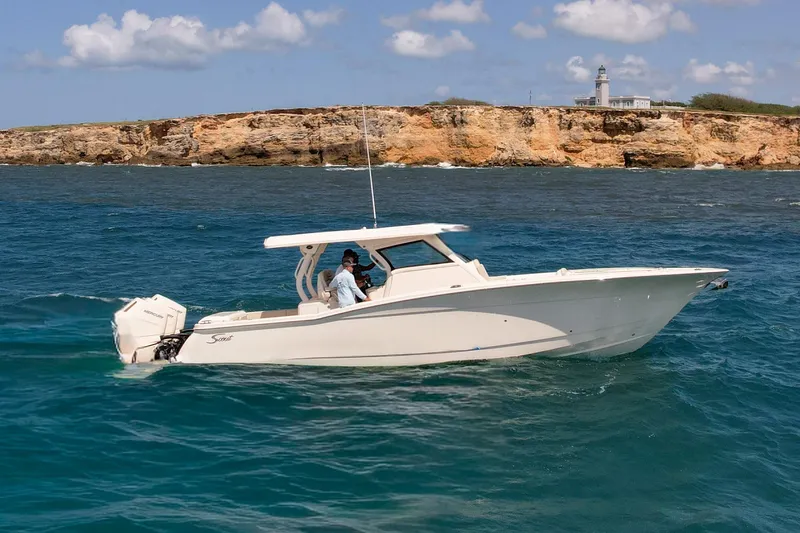  Yacht Photos Pics 2024 Scout 377 LXF boat cruising near rocky coastline with lighthouse in background.