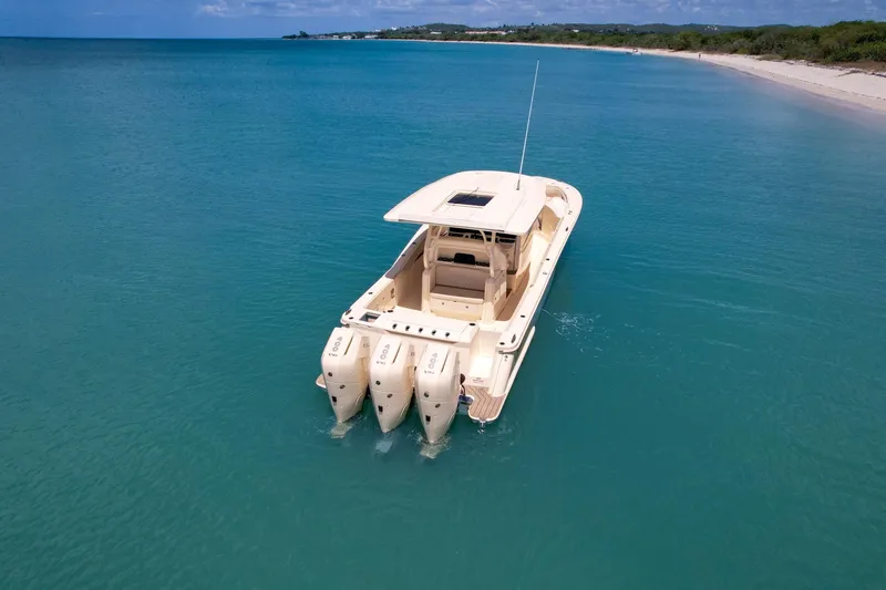  Yacht Photos Pics 2024 Scout 377 LXF boat cruising in clear turquoise waters near a sandy beach.