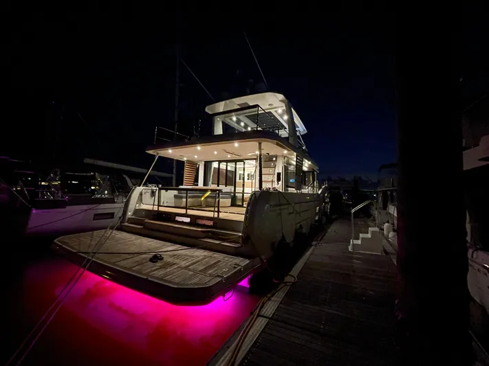  Yacht Photos Pics 2024 Beneteau Grand Trawler 62 docked at night with vibrant underwater lights.