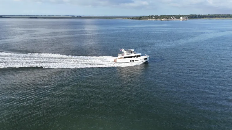  Yacht Photos Pics 2024 Beneteau Grand Trawler 62 cruising on open water, distant shoreline visible.