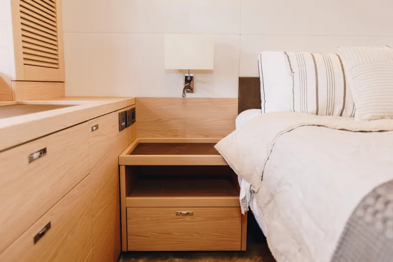  Yacht Photos Pics Luxurious bedroom interior of 2024 Beneteau Grand Trawler 62 with wooden cabinetry and cozy bedding.