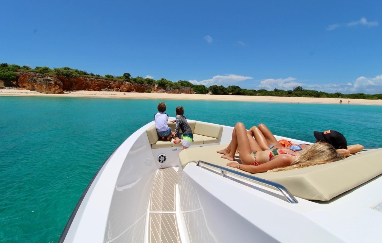 People relaxing on a 2025 Impulse 43 S yacht near a tropical beach.