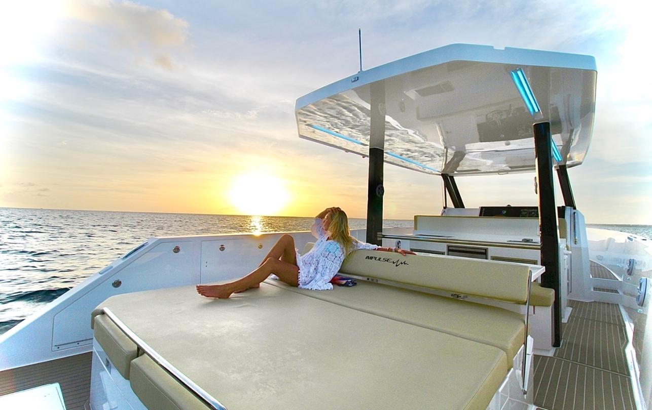 Woman relaxing on 2025 Impulse 43 S yacht at sunset, enjoying ocean view.