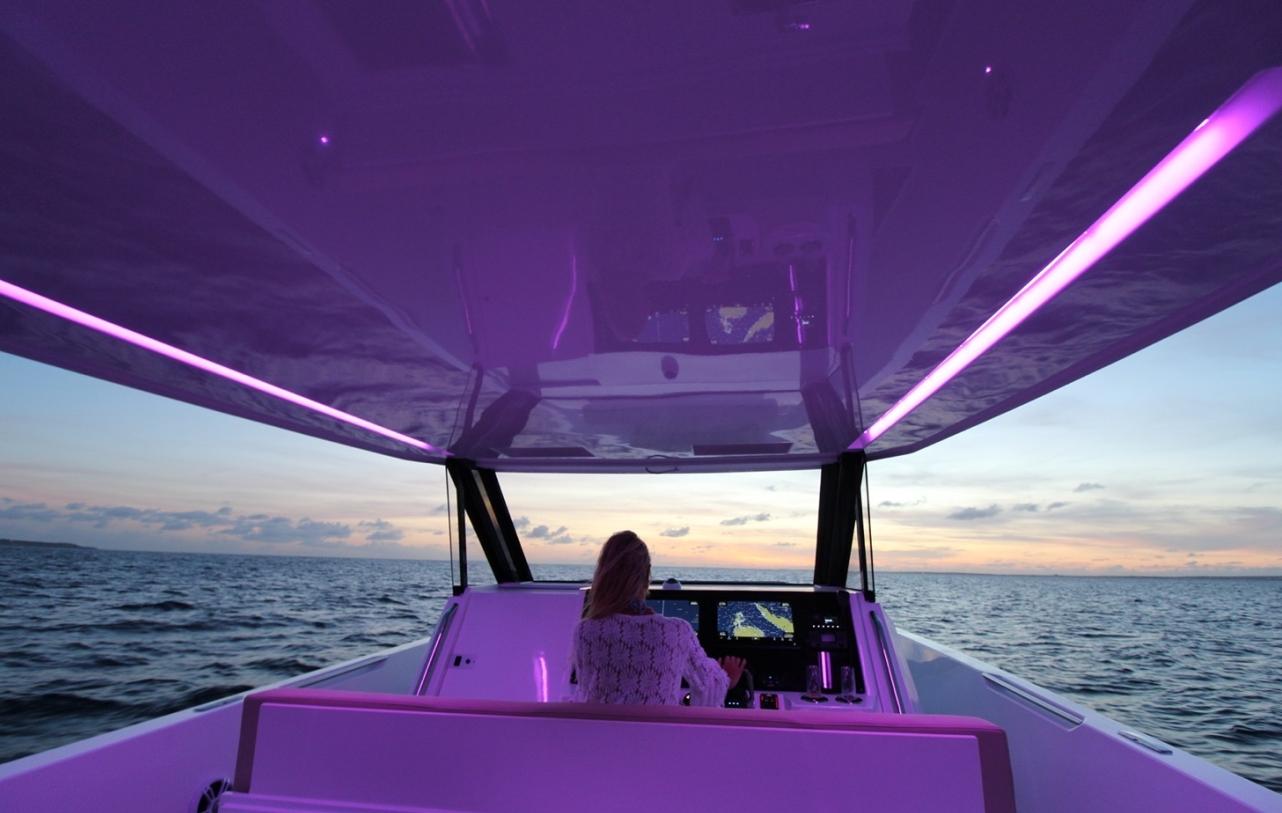 2025 Impulse 43 S yacht interior with purple lighting, navigating at sunset on open water.