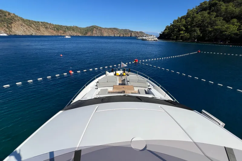 Enough Yacht Photos Pics 2023 Sunseeker 76 Yacht cruising in a scenic coastal bay with clear blue waters.