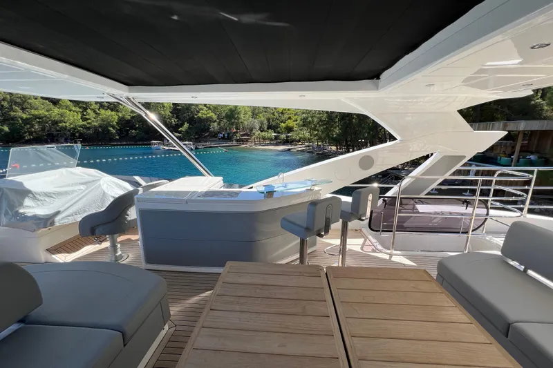 Enough Yacht Photos Pics Luxurious 2023 Sunseeker 76 Yacht deck with seating, overlooking serene blue waters and lush greenery.