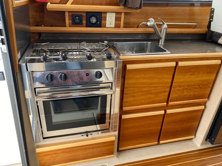  Yacht Photos Pics 2017 Cutwater C-28 boat kitchen with stove, sink, and wooden cabinetry.