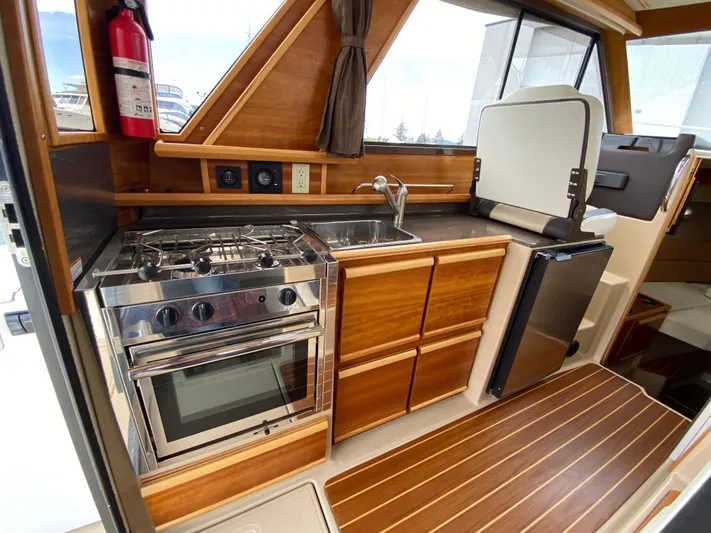  Yacht Photos Pics 2017 Cutwater C-28 boat interior kitchen with stove, sink, and wooden cabinetry.