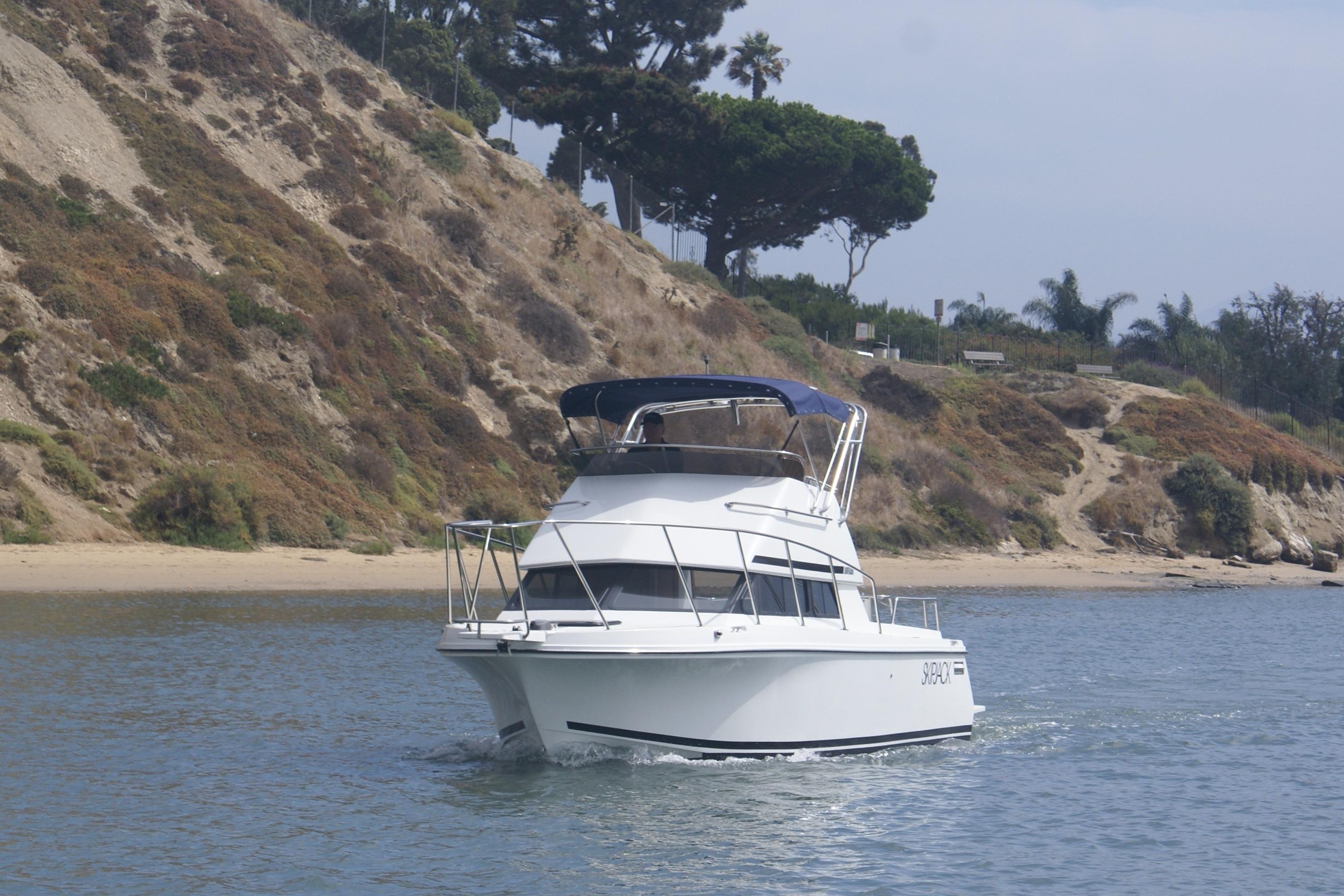 1997 Skipjack 262 Flybridge boat cruising near a rocky shoreline.