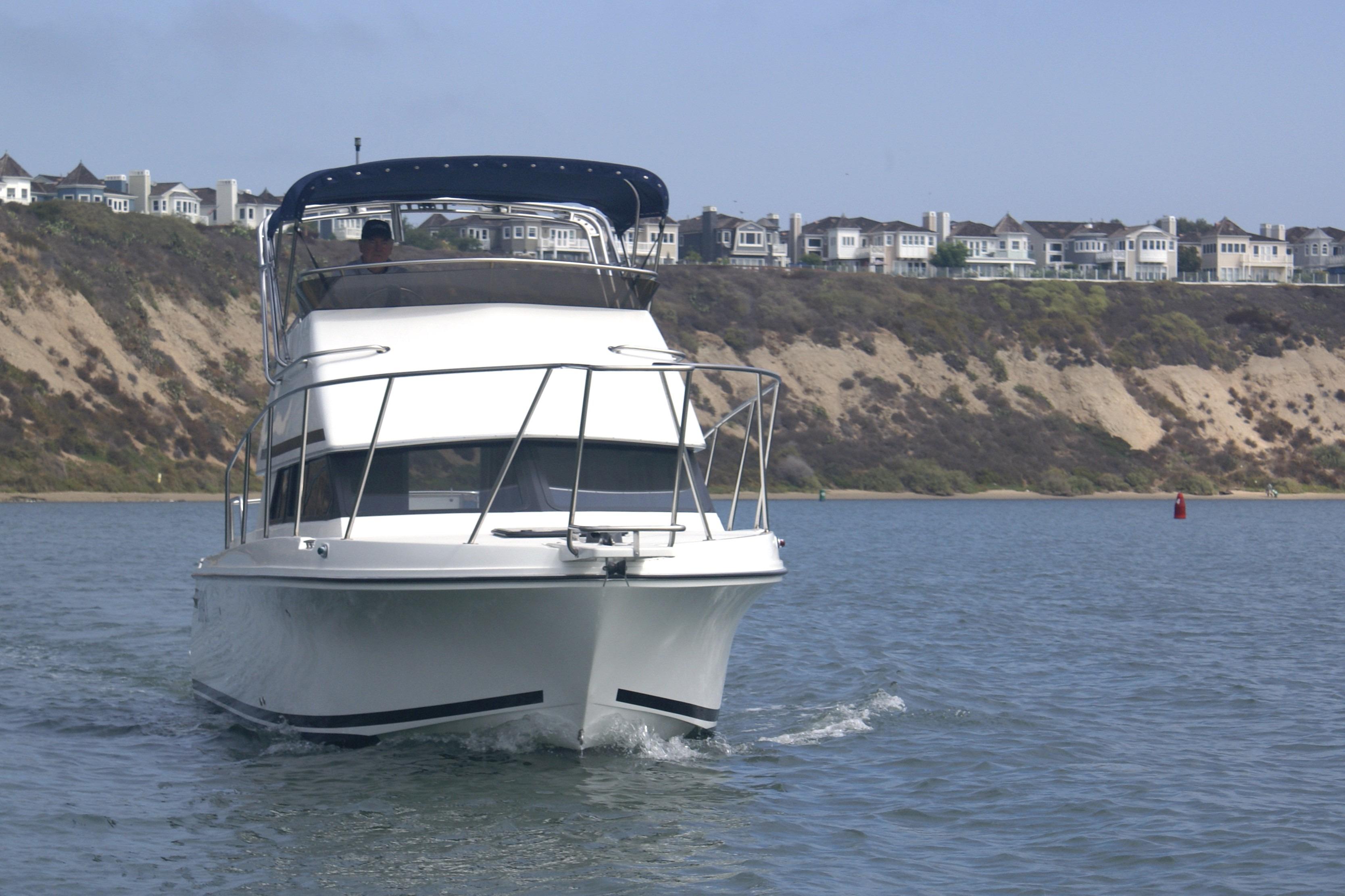 1997 Skipjack 262 Flybridge boat cruising near coastal cliffs and residential area.