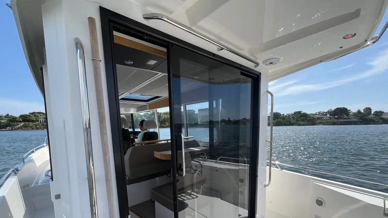 In- Stock 2025 Nimbus C11 #086 Yacht Photos Pics Modern Nimbus Commuter 11 boat interior with glass doors, overlooking serene water and distant shoreline.