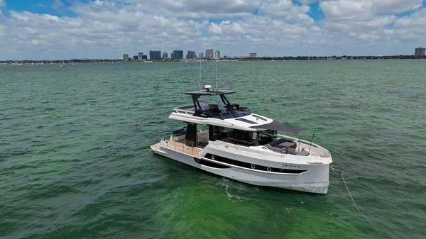  Yacht Photos Pics 2024 OKEAN 52 yacht cruising on a vibrant green sea with city skyline backdrop.